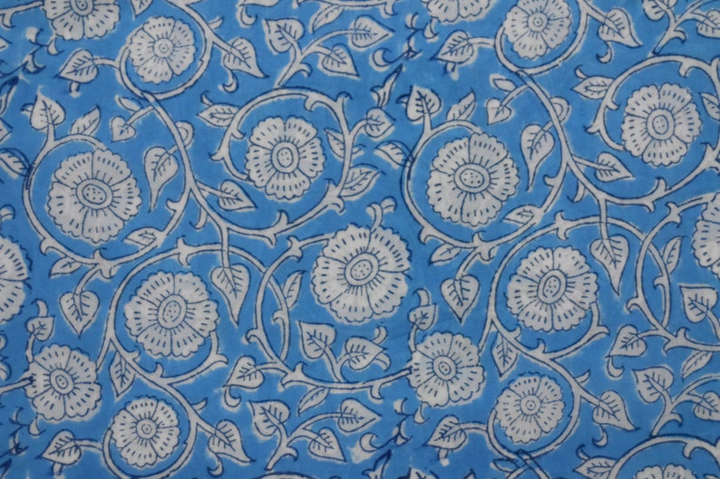 May include: A blue fabric with a white floral pattern. The flowers are stylized and have a simple design. The fabric is perfect for crafting projects or making clothing.