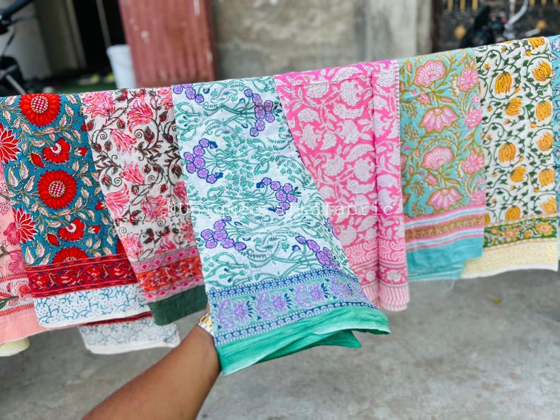 Pu&ograve; includere: Cinque pannelli di tessuto con motivi diversi in vari colori, tra cui rosa, blu, verde e bianco. I pannelli sono appesi a una linea e hanno un design floreale.