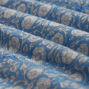 May include: A blue fabric with a white floral pattern. The fabric is folded and has a soft, textured surface.