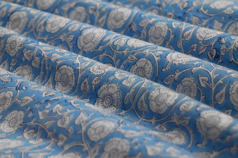 May include: A blue fabric with a white floral pattern. The fabric is folded and has a soft, textured surface.