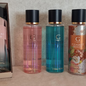 Könnte beinhalten: Ein Geschenkset mit einer Flasche Radiant Sand Duftnebel, drei goldverpackten Pralinen und vier zusätzlichen Duftnebeln in den Düften Oud Elixir, Brilliant Bliss, Pleasant Breeze und Pure Summer. Jede Flasche hat einen schwarzen Deckel.