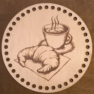 Könnte beinhalten: Ein runder Holz-Stricknadelhalter mit einem Design aus einem Croissant und einer Tasse Kaffee mit aufsteigendem Dampf.