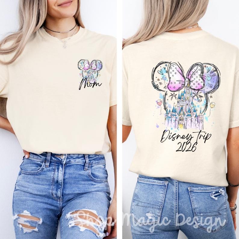 Puede incluir: Camiseta color crema con un dise&ntilde;o colorido de Minnie Mouse. La parte delantera presenta la palabra "Mom" y la trasera dice "Disney Trip 2026". El dise&ntilde;o incluye un castillo y un lazo, con detalles de acuarela.