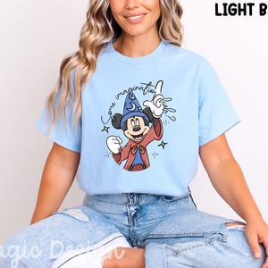 Peut inclure: T-shirt bleu clair avec Mickey Mouse en dessin animé vêtu d'un costume de magicien, avec le texte "Some imagination". Mickey porte un chapeau de magicien bleu et une robe rouge. Le t-shirt est bleu clair.