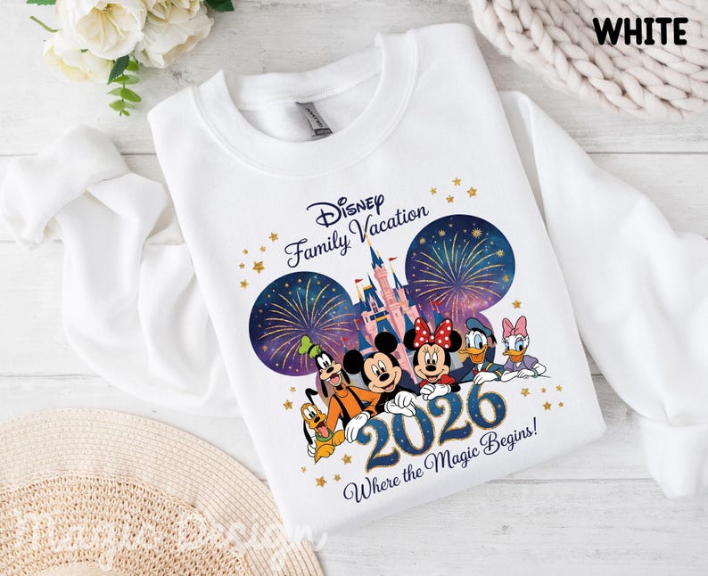 May include: A white crewneck sweatshirt featuring a graphic of Disney characters including Mickey, Minnie, Goofy, Pluto, Donald, and Daisy. The design includes a castle, fireworks, gold stars, and the text Disney Family Vacation 2026 Where the Magic Begins.