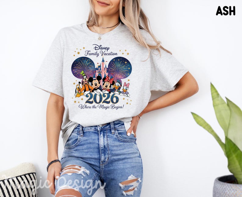 May include: An ash gray short-sleeve t-shirt featuring a graphic of Disney characters including Mickey, Minnie, Goofy, Donald, and Daisy in front of a castle and fireworks. The text reads Disney Family Vacation 2026 Where the Magic Begins.