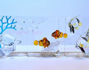 May include: A decorative glass aquarium scene featuring a sea turtle, coral, and various fish. The fish include clownfish with orange and white stripes, and angelfish with black and yellow accents. The coral is a bright blue color.