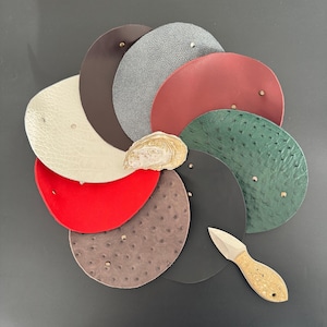 May include: A collection of eight different leather swatches in various colours and textures, including ostrich, stingray, and smooth leather. A small knife with a wooden handle is also included.