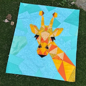 May include: A handmade quilt featuring a giraffe design. The giraffe's head and neck are composed of geometric shapes in shades of yellow, orange, and brown against a light blue background. The quilt is likely made of fabric.