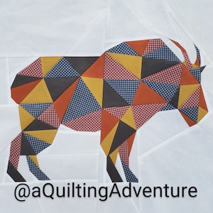 Peut inclure: Un bloc de courtepointe géométrique en patchwork en forme de chèvre de montagne. Le bloc est composé de différents tissus dans des tons de rouge, orange, jaune, bleu et gris. Le bloc est sur un fond blanc. Le texte '@aquiltingadventure' est dans le coin inférieur droit de l'image.