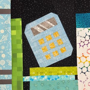 May include: A patchwork quilt square featuring a light blue calculator with yellow buttons. The background is black with white star shapes. Other fabric pieces include green, blue, and white patterns with rockets and chemical structures.