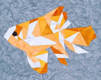 May include: A geometric orange and white fish made of fabric pieces. The fish is on a blue background with a floral pattern.