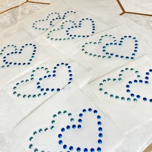 Op de afbeelding: Zeven vellen wit papier met elk een blauw en turquoise strass hart.
