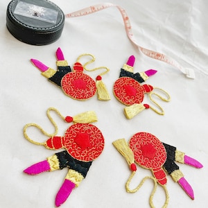 May include: Four red and gold embroidered iron-on patches shaped like lipstick tubes with a round mirror design. Each patch has a gold tassel.