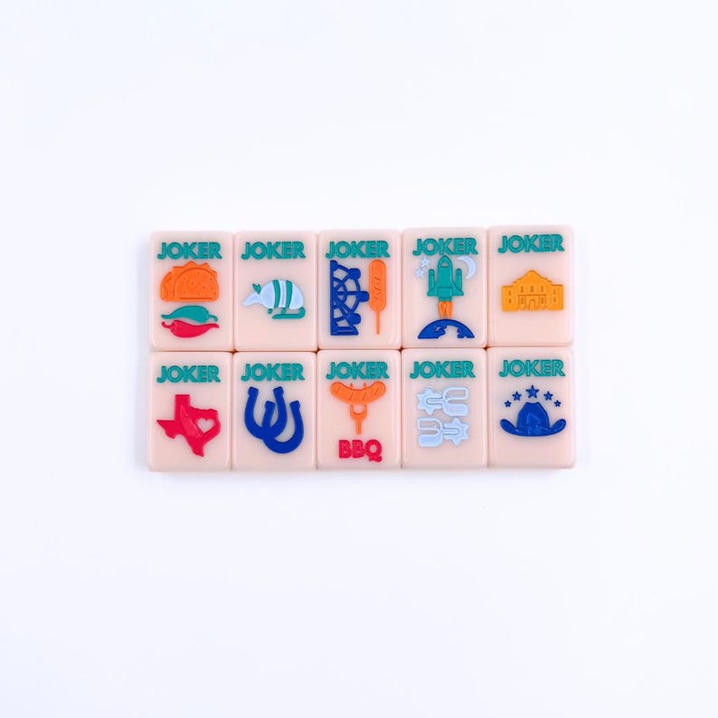 May include: A set of 12 pink dominoes with green, blue, orange, and red illustrations of Texas-themed icons. Each domino has the word "JOKER" printed on it.