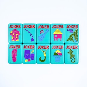 May include: Nine turquoise blue square tiles with the word "JOKER" in red letters on each tile. Each tile has a different colorful graphic design, including a Hawaiian shirt, a ukulele, a tropical hut, a flip-flop, a coffee cup, a fishing hook, a shaved ice dessert, and a lizard.