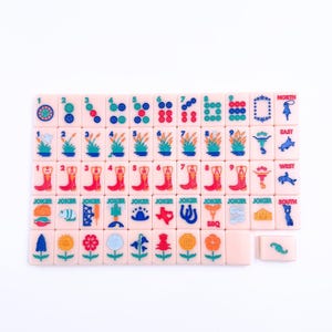 May include: A set of pink and white dominoes with various images, including boots, flowers, and a Texas flag. The dominoes are numbered 1 through 9 and include a Joker tile. The dominoes are arranged in a grid pattern on a white surface.