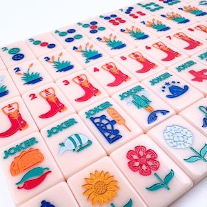 May include: A set of 36 colorful dominoes with various images, including a cowboy boot, a taco, a sunflower, and a rocket ship. The dominoes are made of a light pink plastic and have a white background.