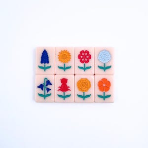 May include: Eight pink tiles with different flower designs. Each tile has a green stem and leaves. The flowers are blue, yellow, red, white, orange, and red.