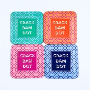 May include: Set of four square coasters with a geometric pattern. Each coaster features the text "CRACK BAM DOT" in white lettering on a different colored background: teal, orange, pink, and blue.