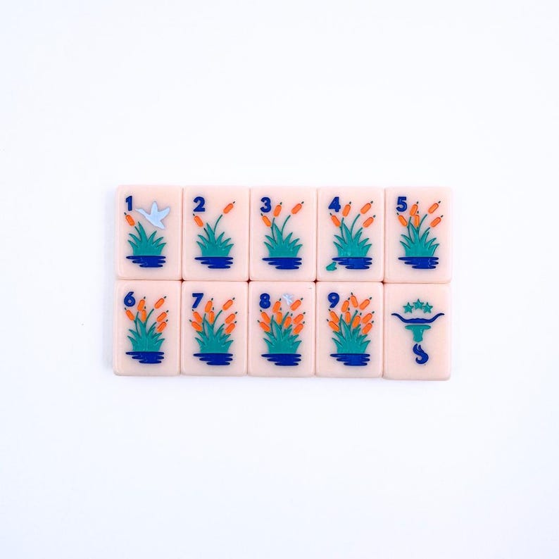 May include: A set of nine pink mahjong tiles with blue and orange designs. The tiles are numbered 1 through 9 and feature a bird and a bull.