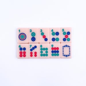 May include: A set of eight pink mahjong tiles with blue and red dots and symbols. The tiles are numbered 1 through 8 and feature a variety of designs, including circles, squares, and stars.