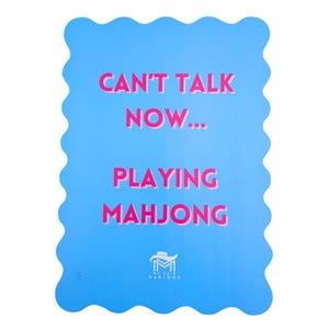 Puede incluir: Una tarjeta azul con un borde ondulado y el texto "Can't talk now... Playing Mahjong" en rosa. La parte inferior de la tarjeta tiene un logotipo para "My Fair Mahjong".