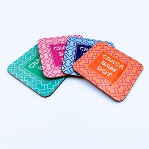 May include: Four colorful coasters with a geometric pattern and the text "Crack Bam Dot" in white. The coasters are made of cork and have a glossy finish.