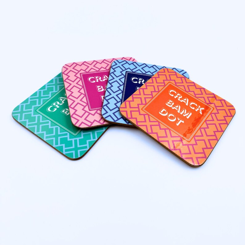 May include: Four colorful coasters with a geometric pattern and the text "Crack Bam Dot" in white. The coasters are made of cork and have a glossy finish.