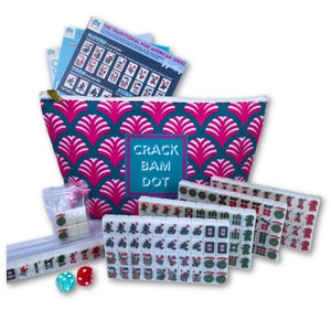 May include: A set of white mahjong tiles with red and green characters and symbols in a teal and pink zippered pouch with the words "Crack Bam Dot" printed on the front. The pouch is decorated with a pink and teal scale pattern. Two red dice and one blue dice are also included.