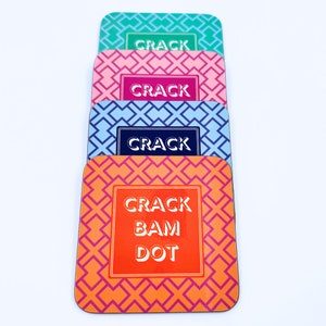 May include: Set of four colorful coasters with a geometric pattern. The coasters feature the text "Crack" and "Crack Bam Dot" in white.