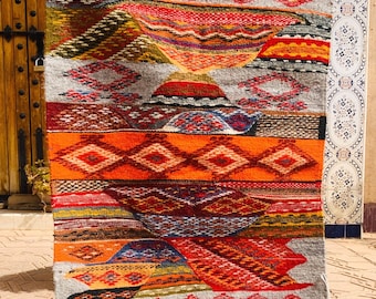 May include: A colorful Moroccan rug with geometric patterns in shades of red, orange, yellow, blue, and green. The rug has a white fringe around the edges.