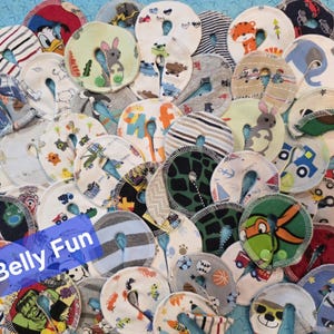 May include: A collection of round, patterned fabric pads with a central opening. The pads feature various colorful designs, including cartoon characters, animals, and vehicles. The text "Belly Fun" is visible on a blue background.
