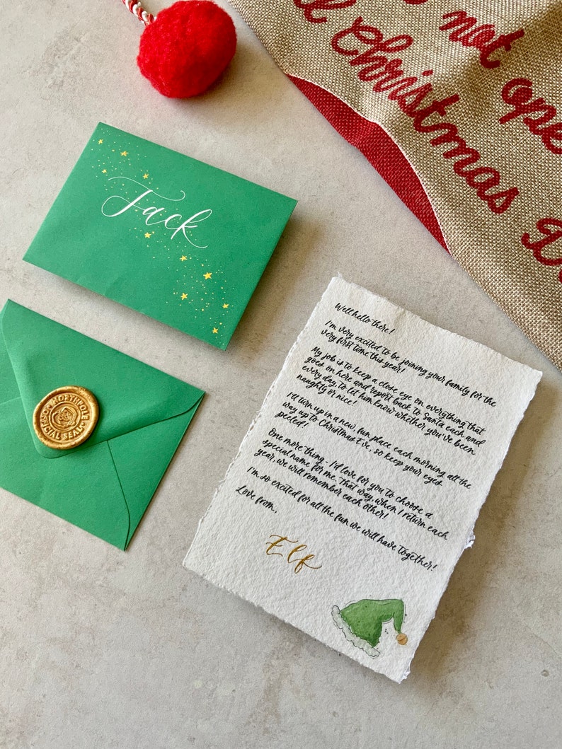 May include: A handwritten letter addressed to Jack from an elf. The letter is written on a piece of parchment paper with a green elf hat illustration at the bottom. The letter mentions keeping a close eye on everything that goes on and reporting back to Santa each day.