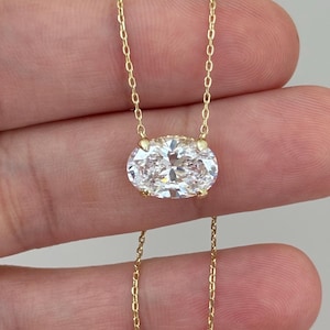 Può includere: Una delicata collana d'oro con un pendente in pietra preziosa trasparente a taglio ovale. Il pendente è sospeso a una sottile catena d'oro. La collana è mostrata su uno sfondo neutro, evidenziando la lucentezza e il design del gioiello. Il pendente misura circa 1,5 cm di lunghezza.