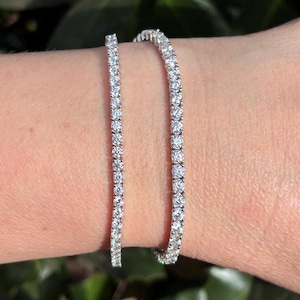 May include: Two silver tennis bracelets with small, clear stones set in a continuous line around the band.