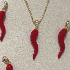 May include: A gold necklace featuring a red horn pendant, accompanied by three additional red horn pendants. The pendants have gold bails adorned with small, clear stones. The background displays the text "RaffEssentials".