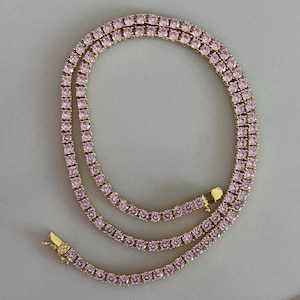 May include: A gold-toned necklace with pink gemstones. The necklace is composed of multiple strands of small, square-cut pink stones, creating a continuous, sparkling effect. The clasp is visible at the end of the necklace.