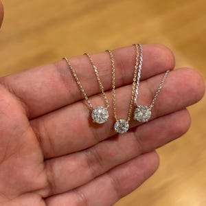 May include: Three delicate necklaces with round, clear gemstones. Two have gold chains, and one has a silver chain. The gemstones are set in simple, classic settings. The necklaces are displayed against a neutral background.