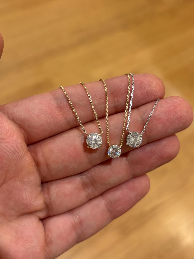 May include: Three delicate necklaces with round, clear gemstones. Two have gold chains, and one has a silver chain. The gemstones are set in simple, classic settings. The necklaces are displayed against a neutral background.