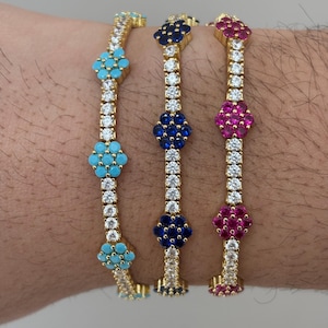 May include: Three gold-toned bracelets with different colored gemstones. One bracelet has turquoise stones, another has dark blue stones, and the third has pink stones. Each bracelet features a line of clear, sparkling stones.