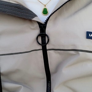 May include: A beige jacket with a black zipper and a green jade pendant necklace. The necklace has a gold chain and a small, green jade pendant in the shape of a Buddha.