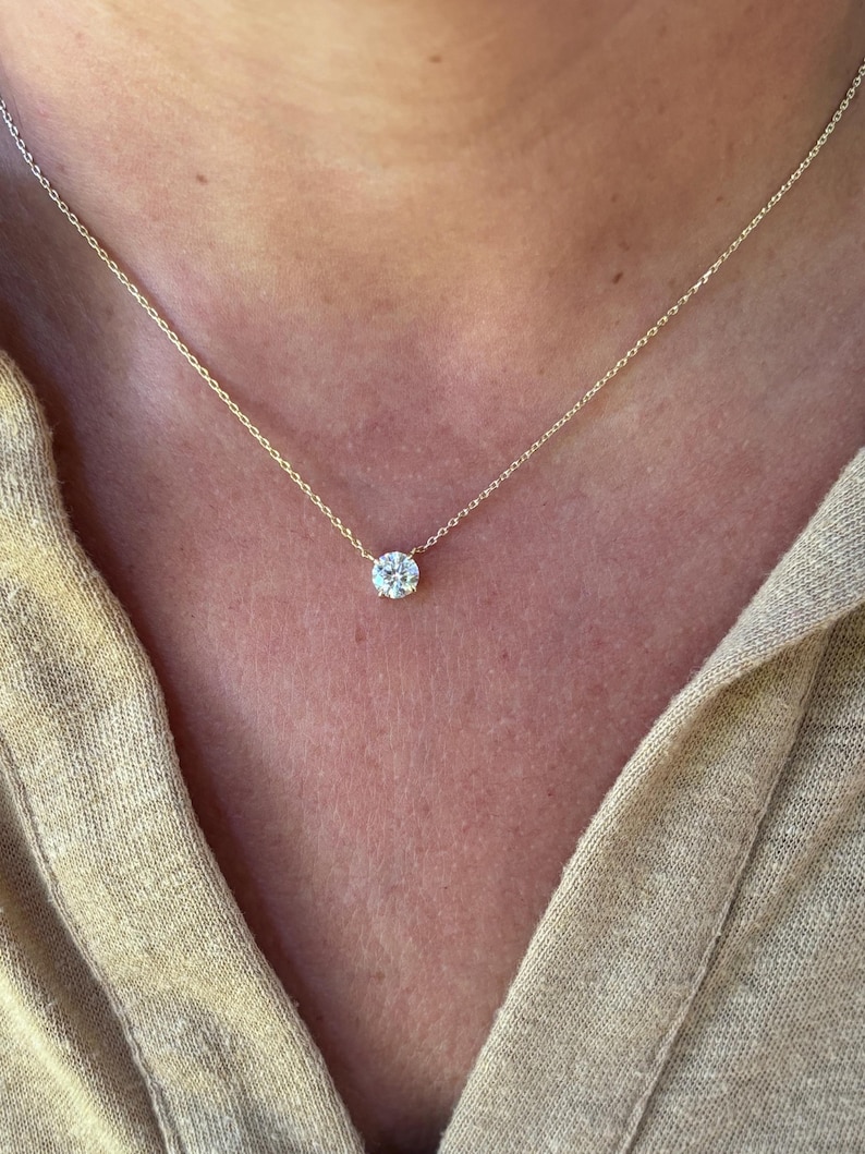 May include: A delicate gold necklace featuring a single, round, sparkling diamond pendant. The diamond is set in a simple, classic design, suspended from a fine gold chain. The necklace is shown against a neutral background.
