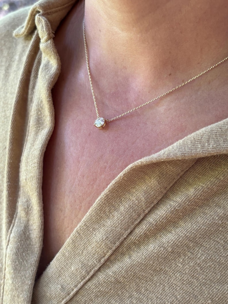 May include: A delicate gold necklace featuring a single, round, clear gemstone pendant. The pendant is set in a gold bezel and hangs from a thin gold chain. The necklace is shown against a neutral background.