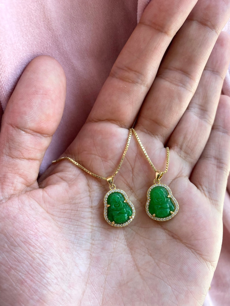 May include: Two gold necklaces with green jade pendants featuring a carved laughing Buddha design. Each pendant is surrounded by a row of clear cubic zirconia stones.