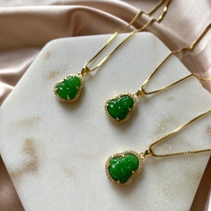 May include: Three gold necklaces with green jade pendants shaped like the Chinese deity Hotei, also known as the Laughing Buddha. Each pendant is surrounded by a halo of small clear rhinestones.