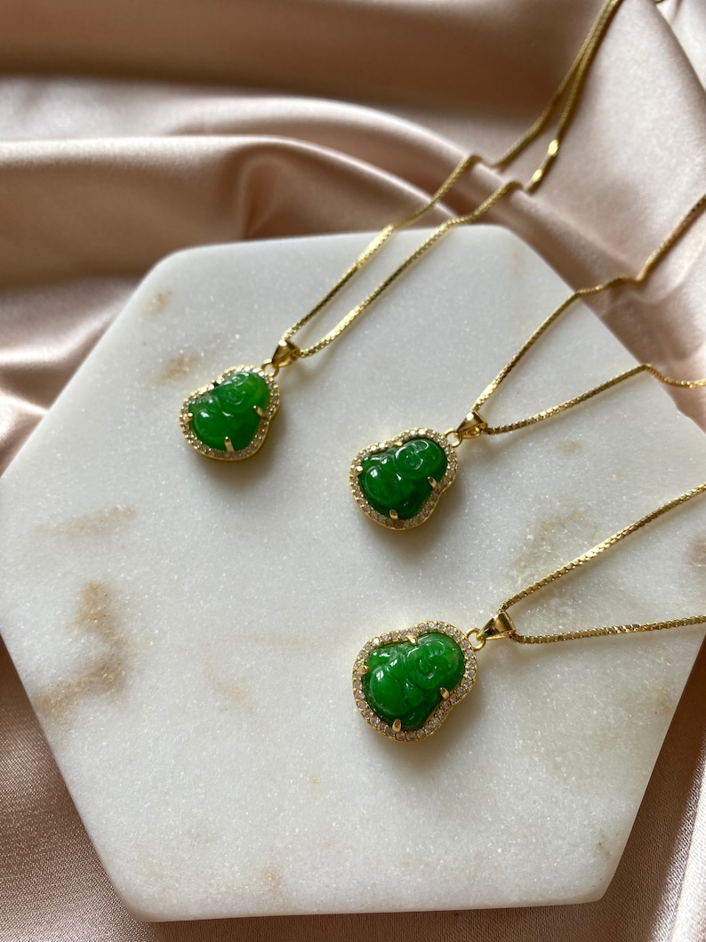 May include: Three gold necklaces with green jade pendants shaped like the Chinese deity Hotei, also known as the Laughing Buddha. Each pendant is surrounded by a halo of small clear rhinestones.