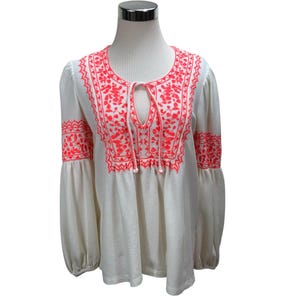 May include: White long-sleeve blouse with bright coral embroidery. The blouse features a round neckline, a keyhole opening, and balloon sleeves. The embroidery is detailed and covers the neckline, chest, and sleeves. The fabric has a subtle striped texture.