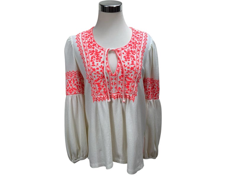May include: White long-sleeve blouse with bright coral embroidery. The blouse features a round neckline, a keyhole opening, and balloon sleeves. The embroidery is detailed and covers the neckline, chest, and sleeves. The fabric has a subtle striped texture.