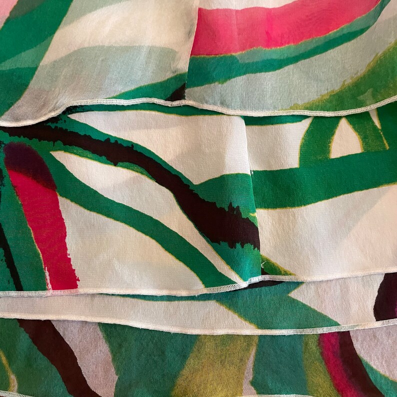 Peut inclure: Gros plan sur un tissu blanc avec des motifs abstraits verts, noirs et roses. Le tissu est superpos&eacute; et pr&eacute;sente un bord festonn&eacute;.